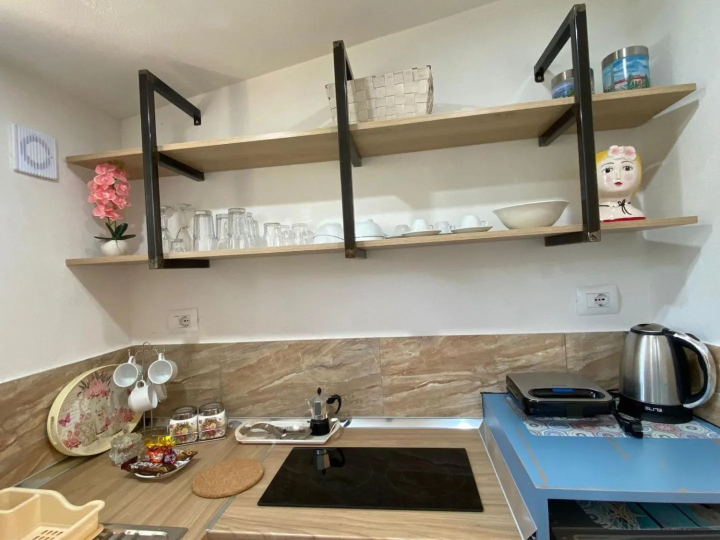 Kitchenette at Areti Rooms Hotel with open oak shelves, glassware, a moka pot, kettle and hob