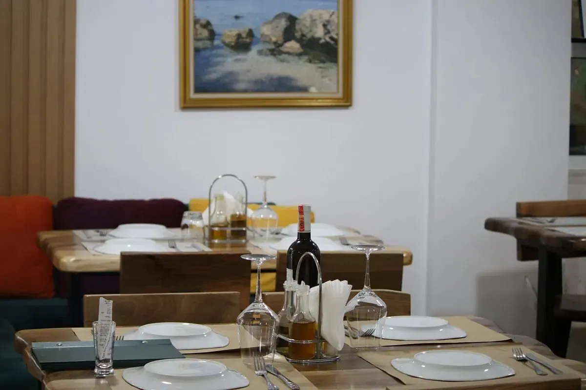 Laid tables in front of a banquette upholstered in orange, burgundy and mustard, beneath a gold-framed painting of rocks in shallow water