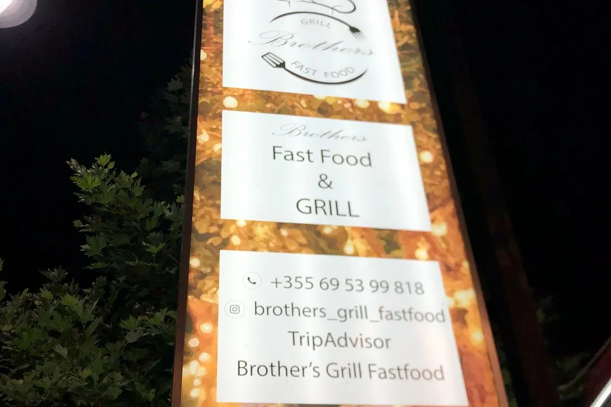 The illuminated Brothers Grill & Fast Food sign at night, three white panels on a gold ground