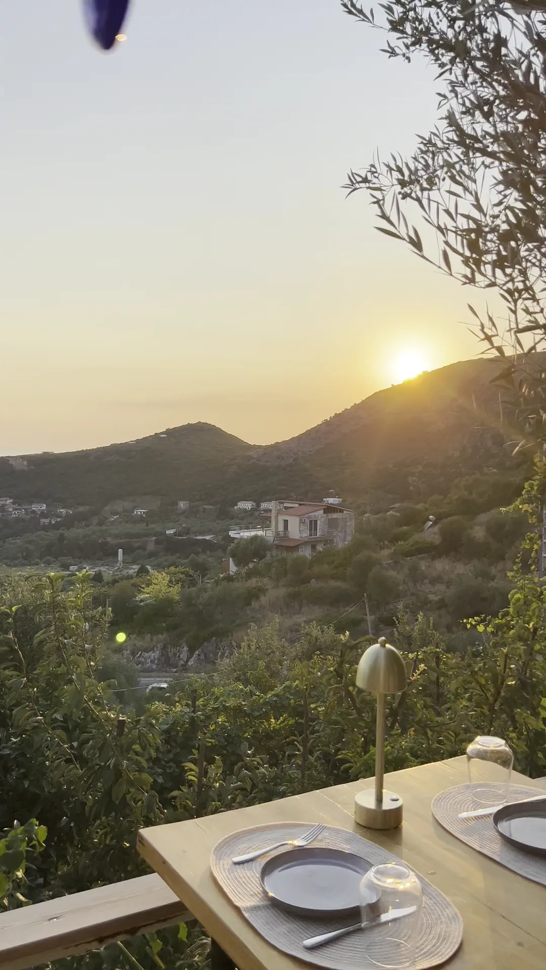 Sun dropping behind the ridge across the valley, seen over a set table on the Fig & Olive terrace