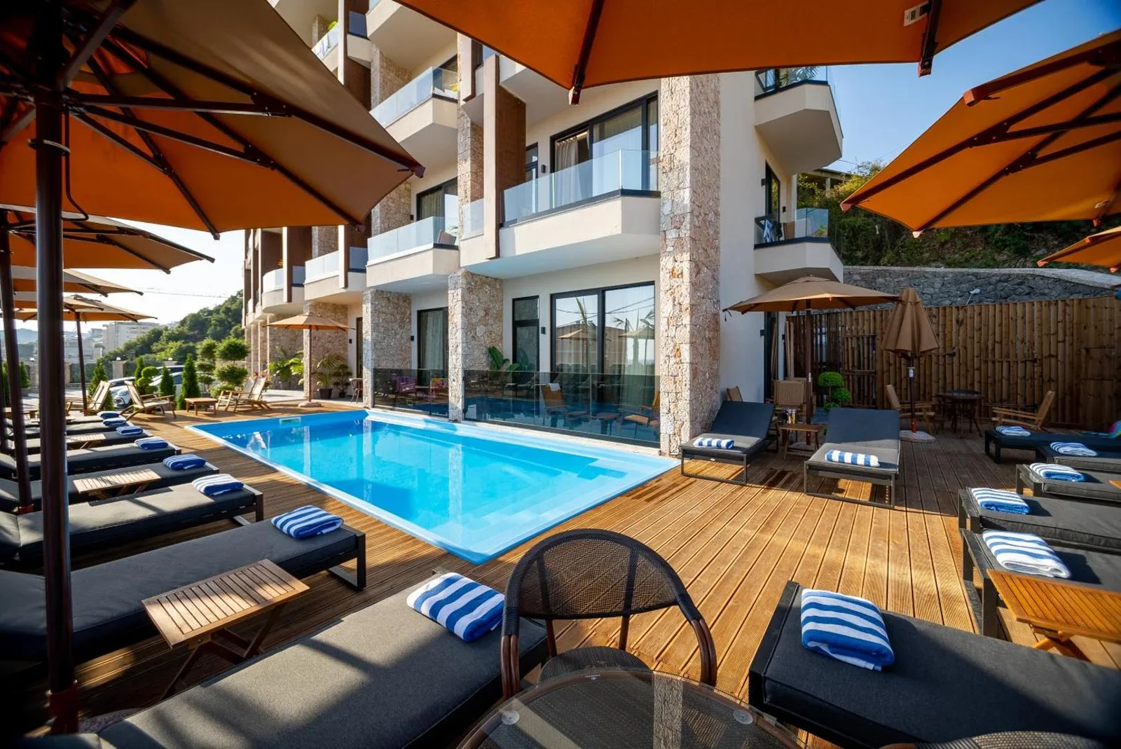 The pool at Hotel Potami on its timber deck, loungers with folded blue-and-white striped towels under orange parasols alongside