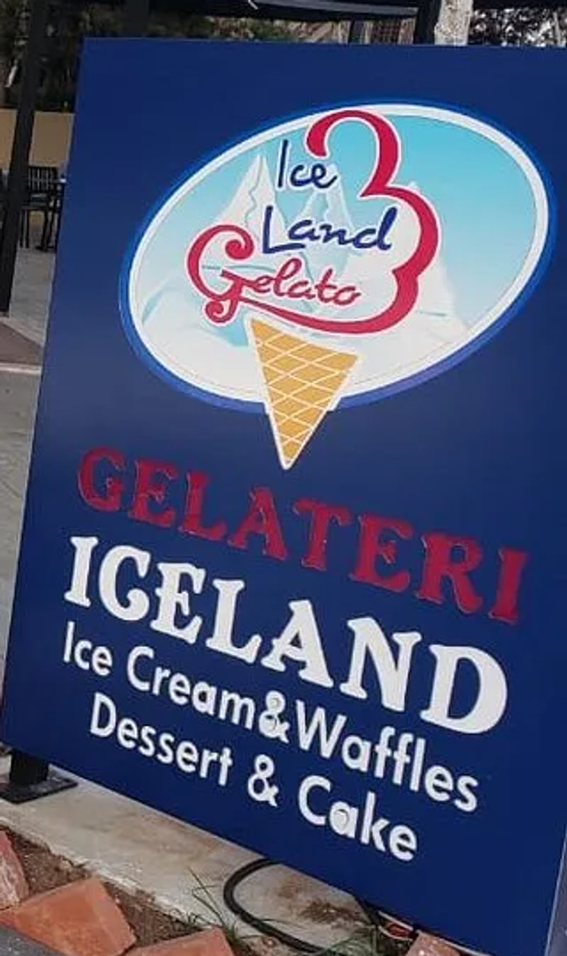 A navy board standing at the pavement, lettered GELATERI ICELAND, Ice Cream and Waffles, Dessert and Cake