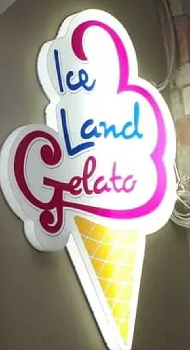 An illuminated sign cut in the shape of an ice cream cone, lettered Ice Land Gelato in blue and magenta