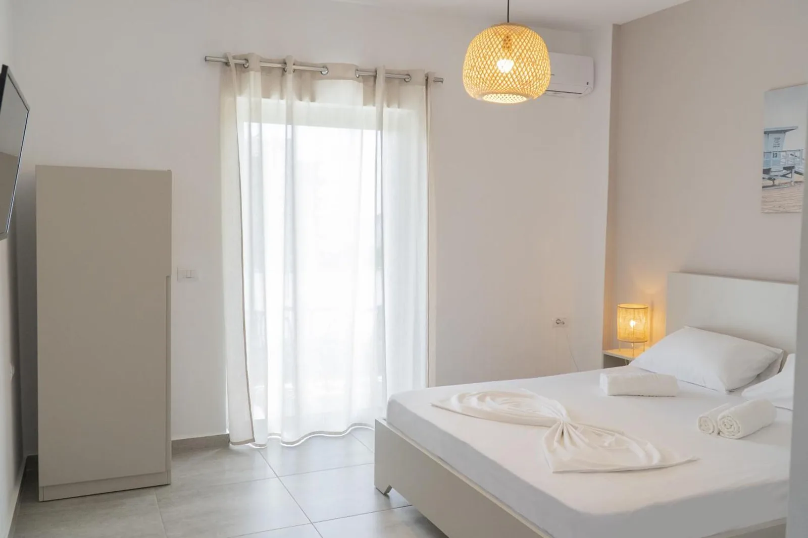 A white double room with a full-height balcony door, wardrobe and air conditioning