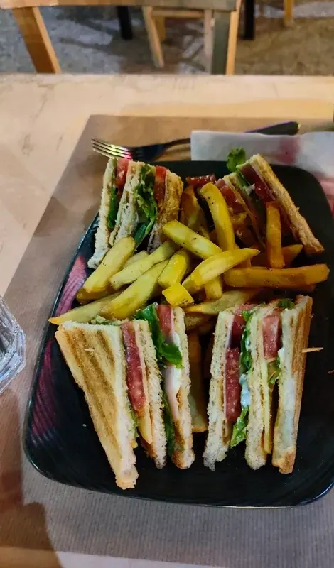 Four quarters of a toasted club sandwich stood on end around a pile of thick-cut chips on a black rectangular plate