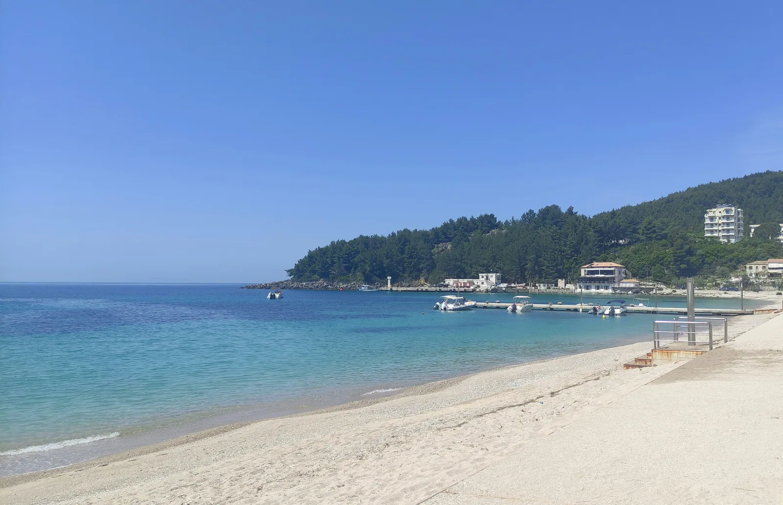 Spile bay in Himarë, its jetty and the pine headland — the town the restaurant stands in, not the restaurant