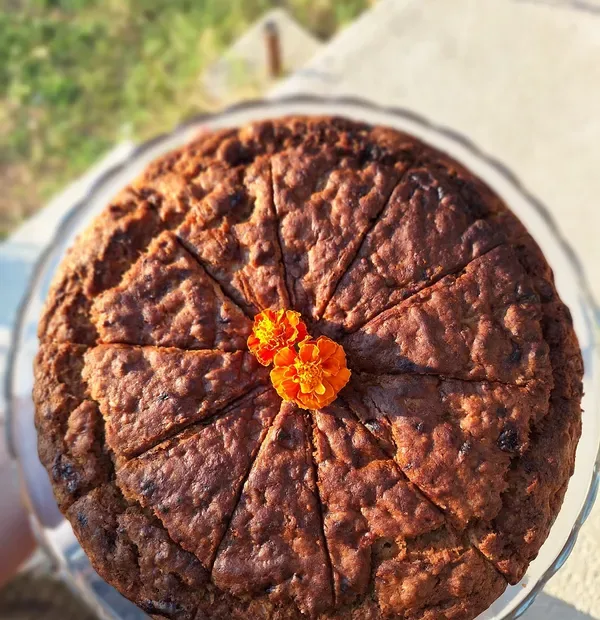 A whole spiced cake on a glass stand, cut into wedges and topped with two marigolds