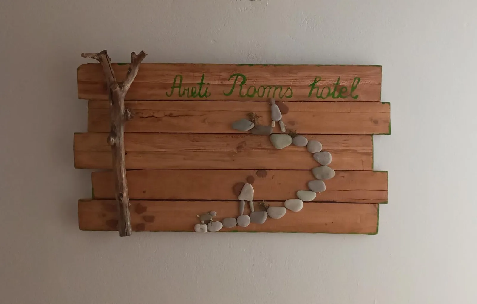Hand-painted plank sign reading Areti Rooms hotel in green script, with a driftwood branch and a pebble mosaic