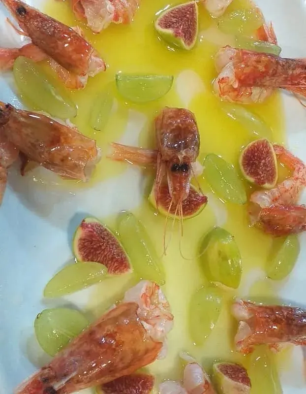Prawns arranged with quartered figs and green grapes in a pool of olive oil on a white plate