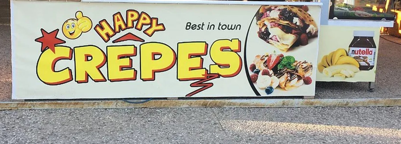 The crepe counter standing out on the paving, its printed banner running the length of the front, a smaller printed panel of a chocolate-spread jar and bananas at the far end, and a glass display case beyond that.