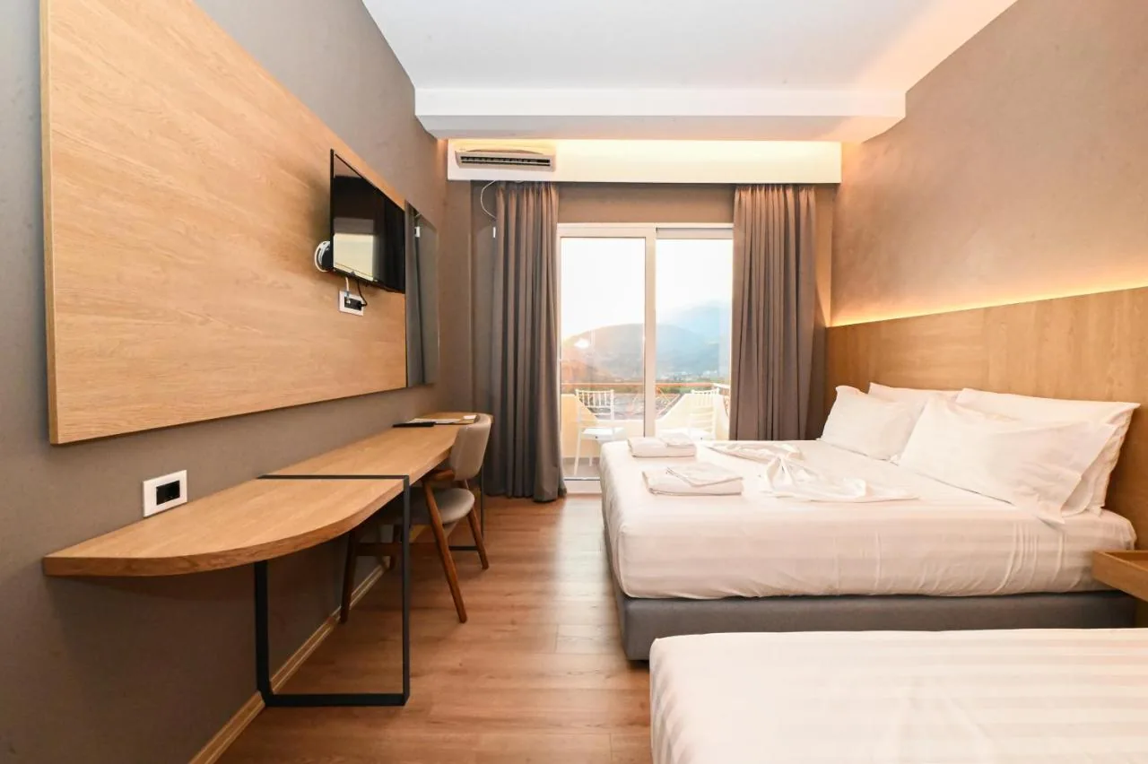 A refitted bedroom with an oak-panelled wall, a wall-mounted television, a long desk and a glazed balcony door showing hills and haze.