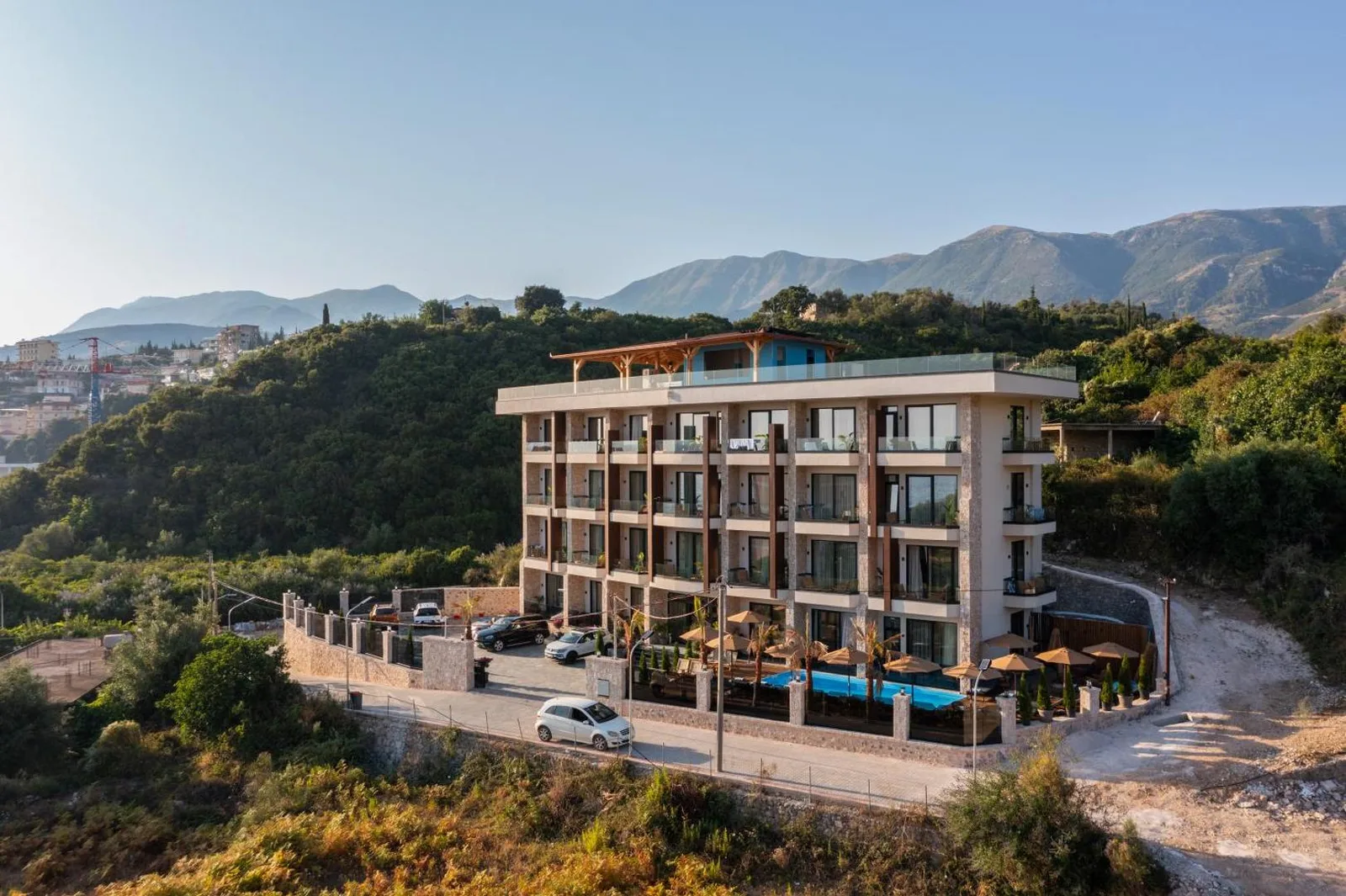 Hotel Potami seen from the air on its hillside plot above Potam, with the pool deck along the near side and the Ceraunian ridge behind