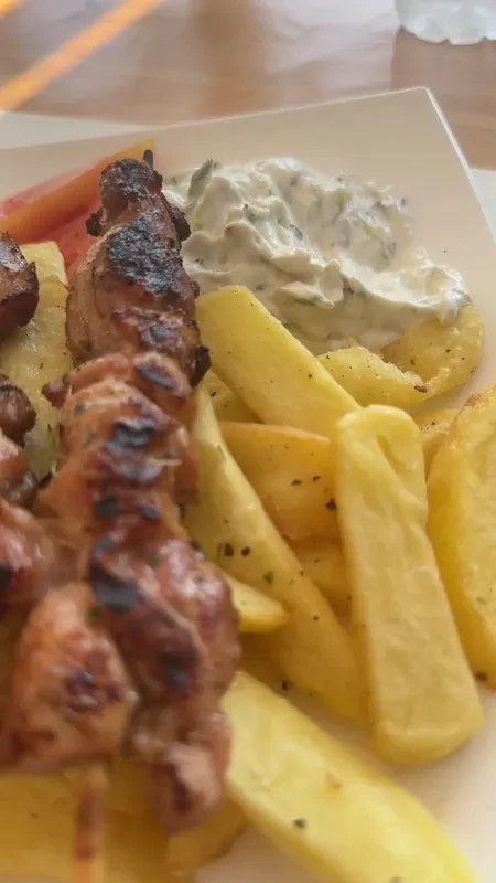 Charred chicken skewers on a plate with thick-cut chips and tzatziki