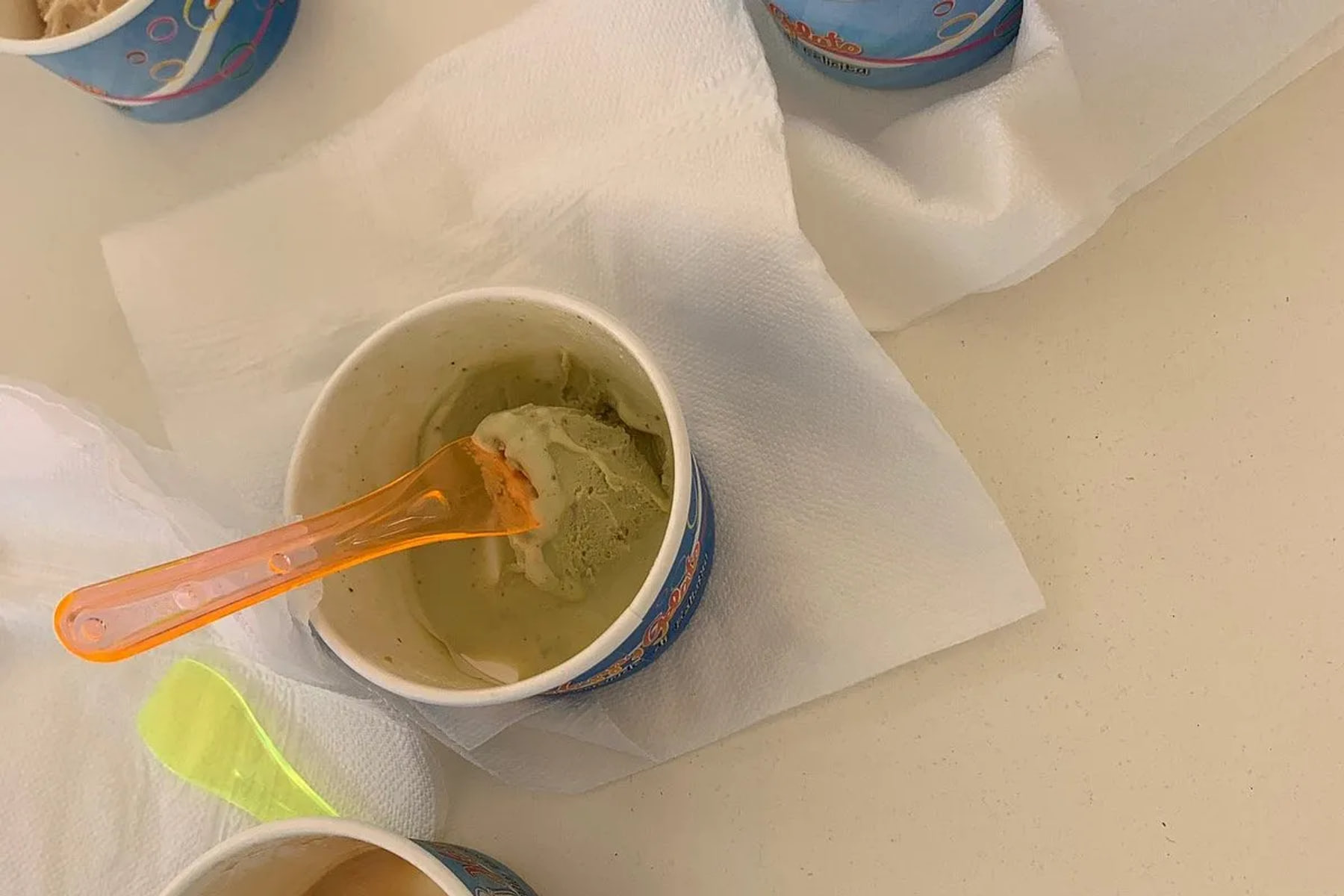 Cups of scooped gelato on a pale table, coloured plastic spoons and paper napkins with them