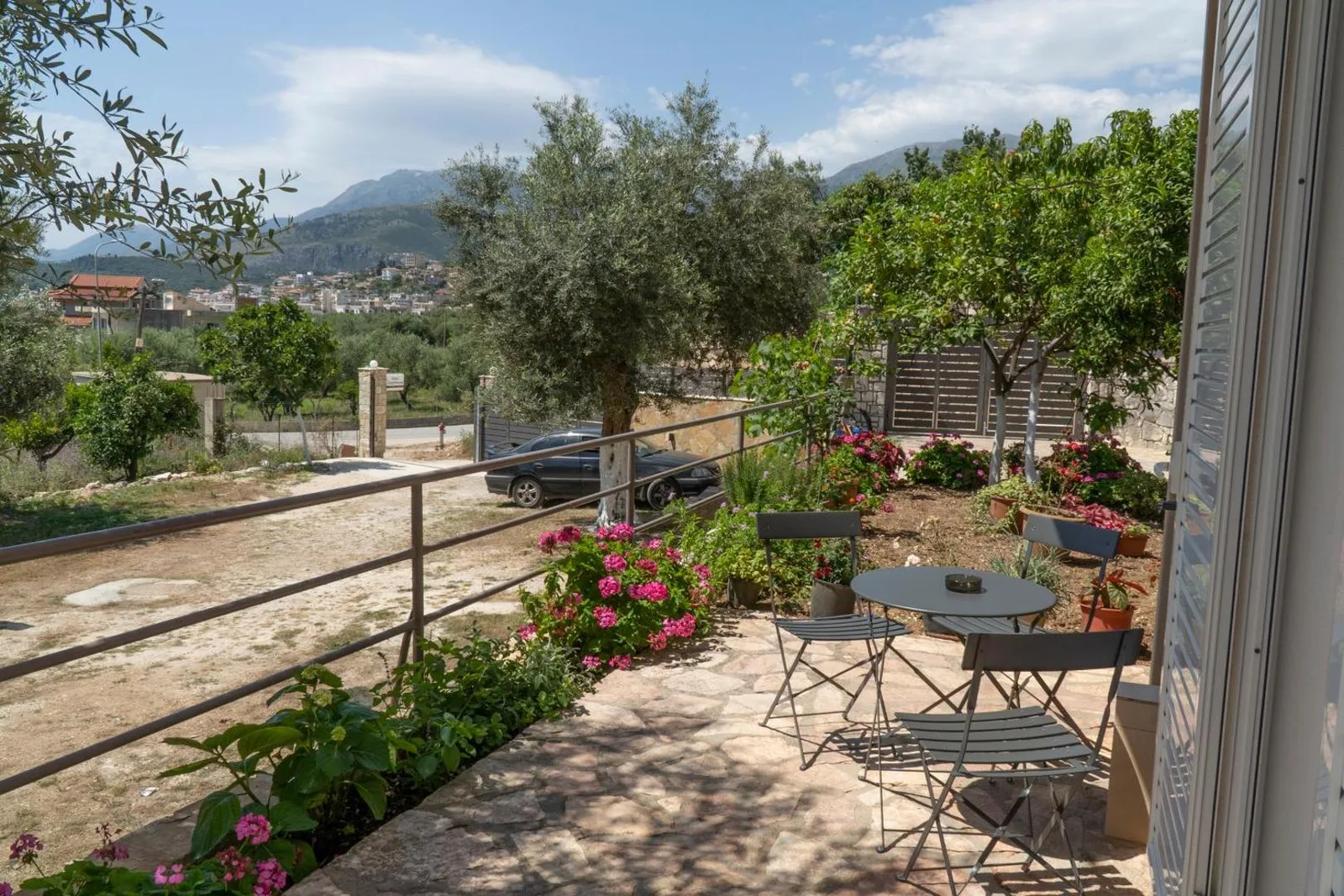 A flagstone garden terrace with a table, looking past olive and citrus trees to the mountains