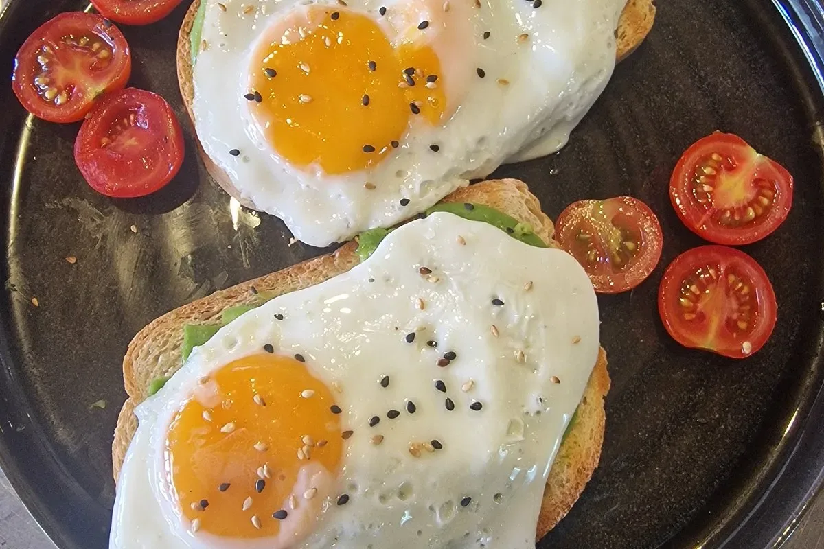 Two fried eggs on toasted bread with avocado and halved cherry tomatoes, on a dark plate at Lido Lounge