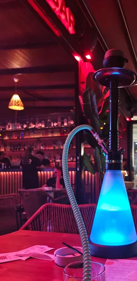 Red neon sign over the bar at Lido Lounge, a lit shisha pipe on the table and the amber-lit counter front behind