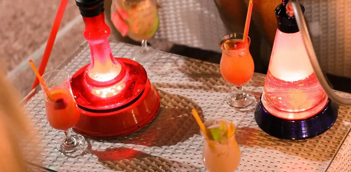 Two lit shisha pipes and cocktails on a glass-topped table at Lido Lounge, Himarë