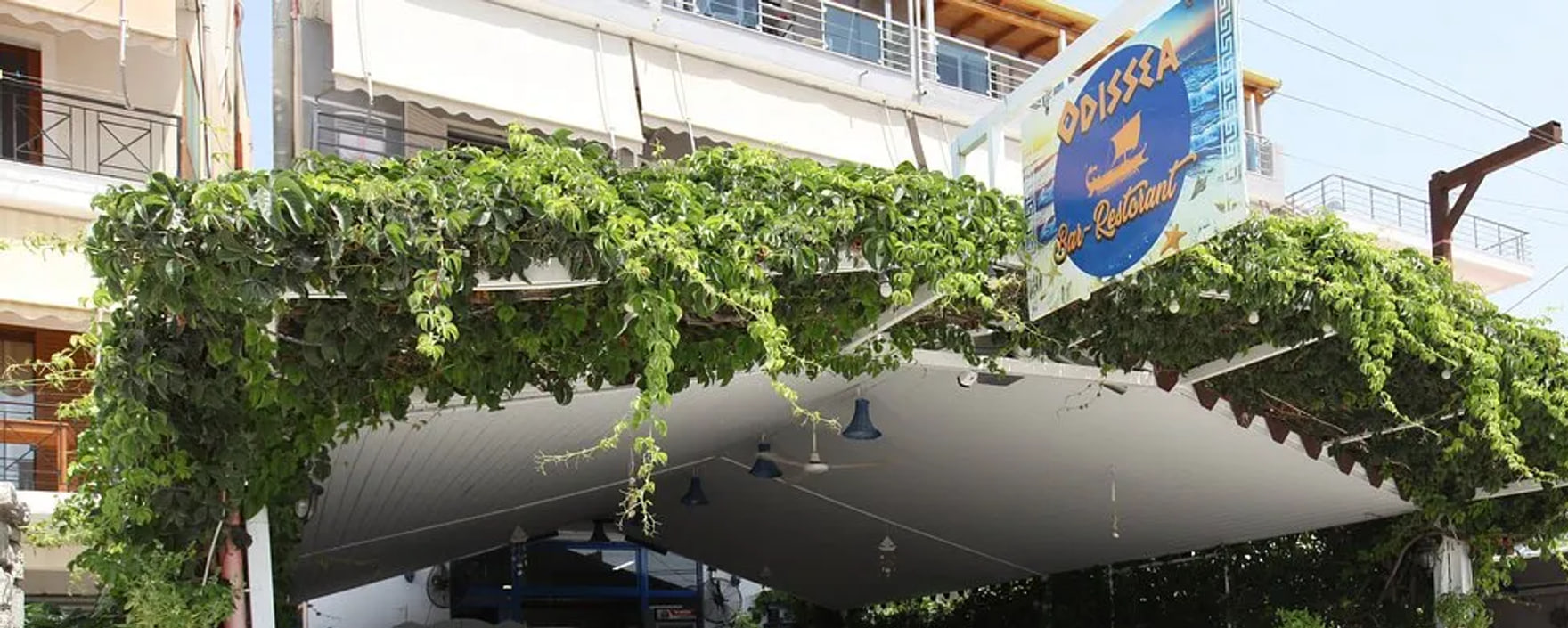 The creeper-covered pergola over the front of Restaurant Odissea, with the round Odissea Bar-Restorant sign above it