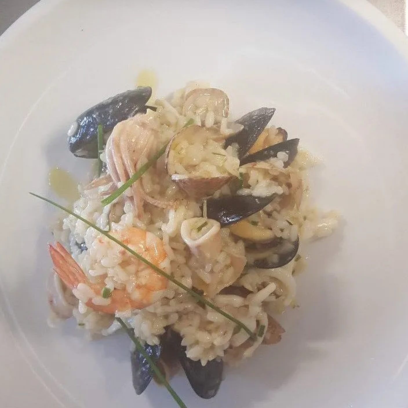 A plate of seafood risotto with mussels, prawns, clams and squid, finished with chives