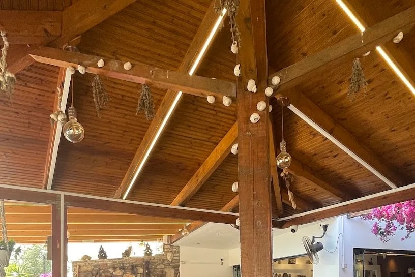 The pitched timber roof of the dining room at Taverna Velco, hung with dried herbs, strings of garlic and filament bulbs