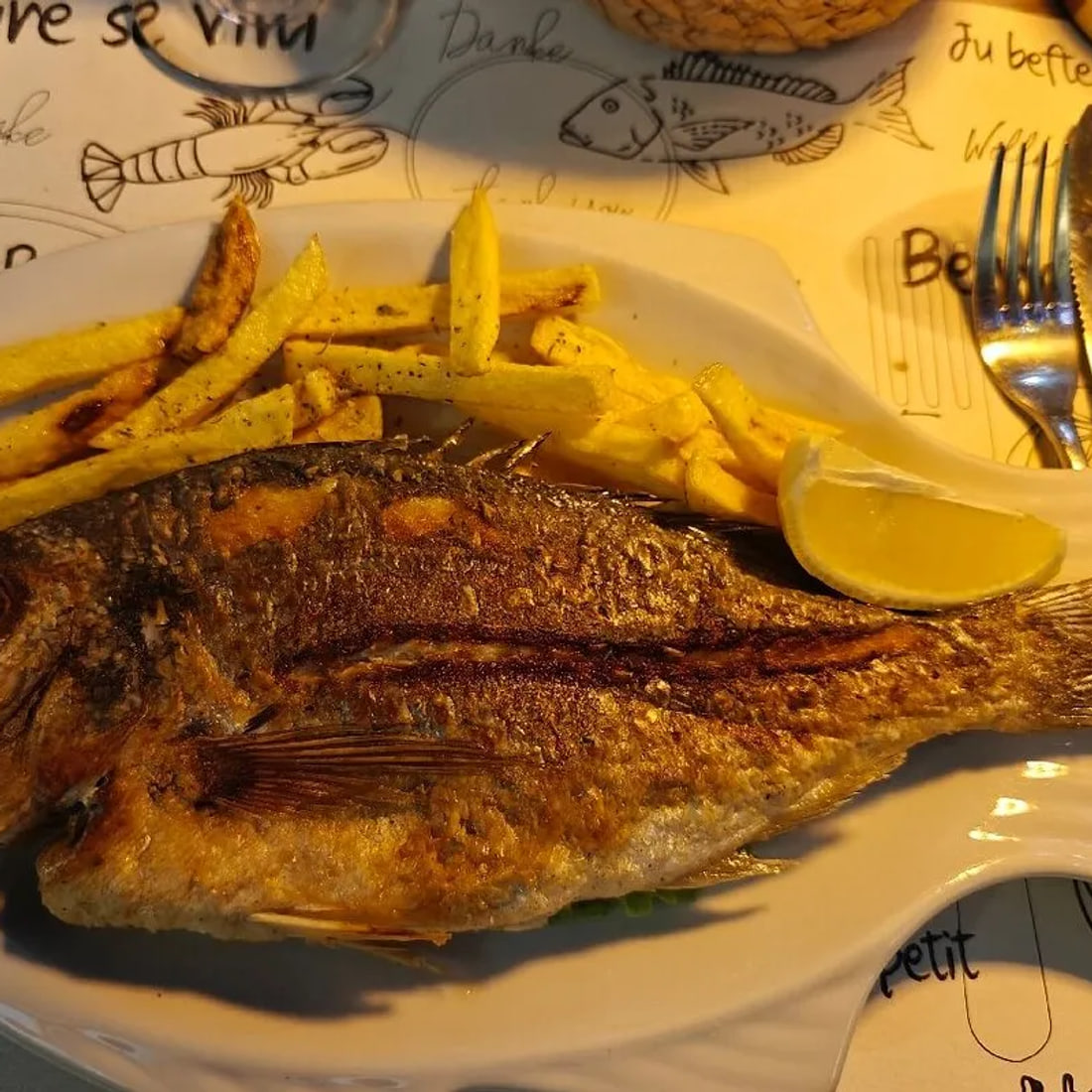 A whole grilled fish with chips and lemon, close