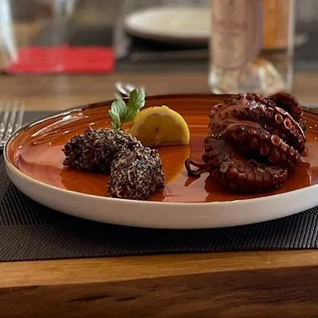 Grilled octopus with lemon and two dark grain croquettes on a copper-glazed plate, close
