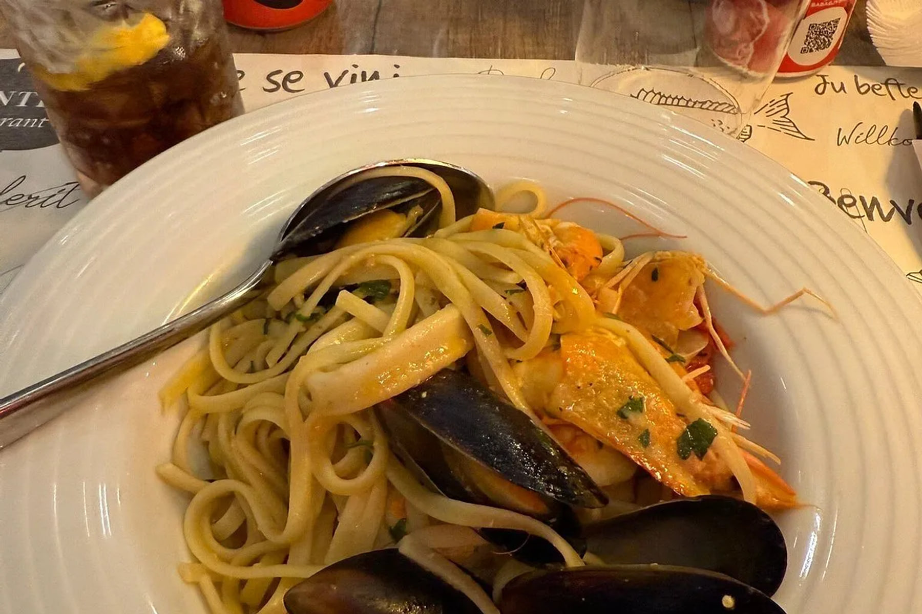 Linguine tossed with mussels, prawns and squid in a shallow white bowl on the printed placemat