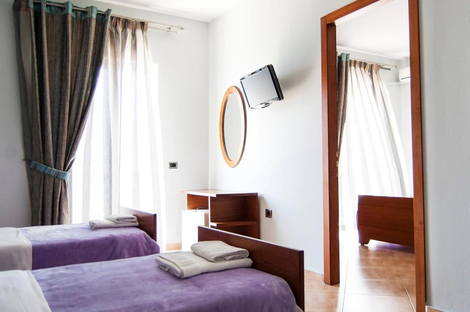 Two beds under purple throws beside a full-length mirror, with a doorway through to a second bedroom
