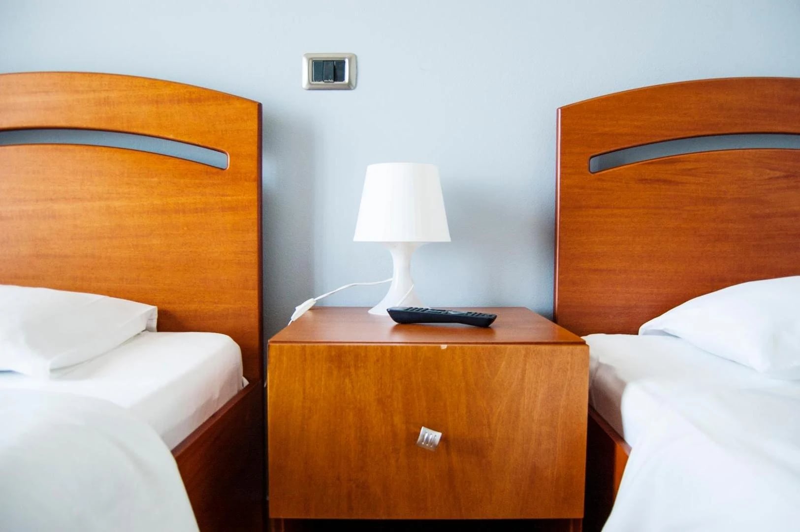 Two single beds either side of a cherry-wood cabinet with a lamp and a remote