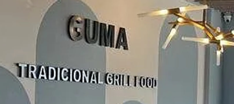 Lettering mounted on the dining-room wall reading GUMA above TRADICIONAL GRILL FOOD, a brass fitting lit at the right