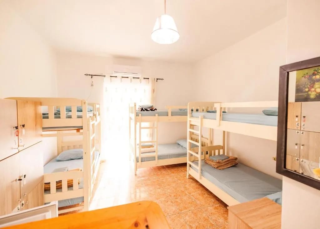 A mixed dormitory at Oasis Hostel with pine bunk beds, tiled floor, a wall of lockers and an air-conditioning unit