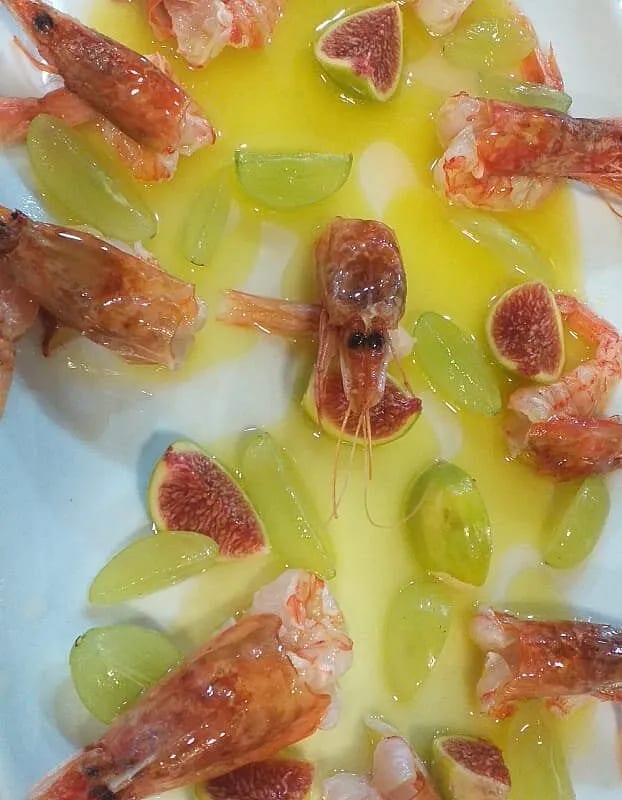 Prawns arranged with quartered figs and green grapes in a pool of olive oil on a white plate