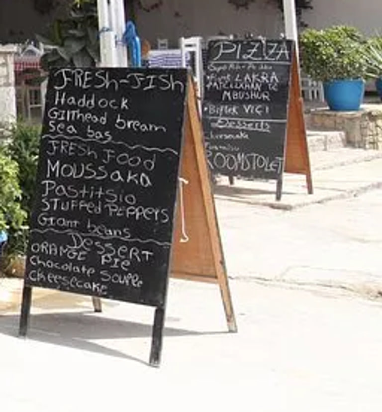 Two handwritten chalkboards standing on the pavement outside the restaurant, one headed Fresh-Fish and one headed Pizza