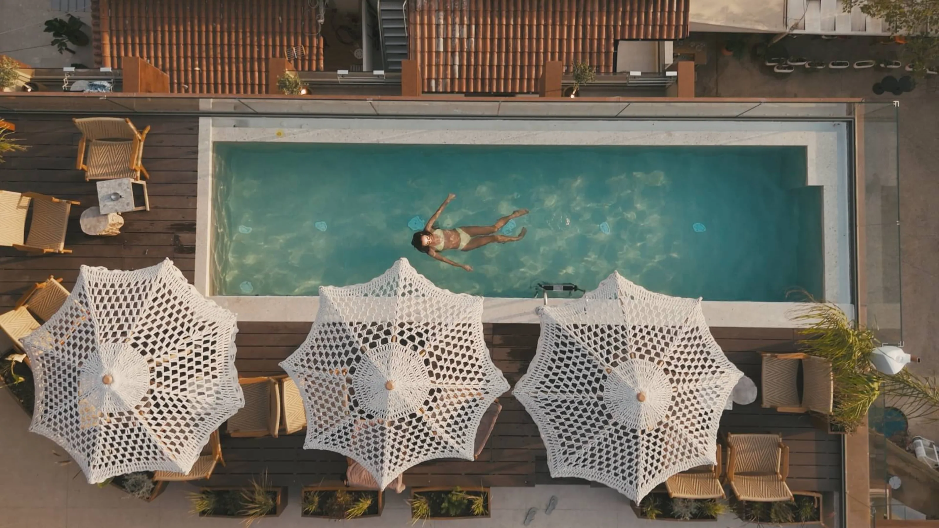 The rooftop pool at Saint Nicolas Hotel from directly above, with three crocheted parasols along the deck