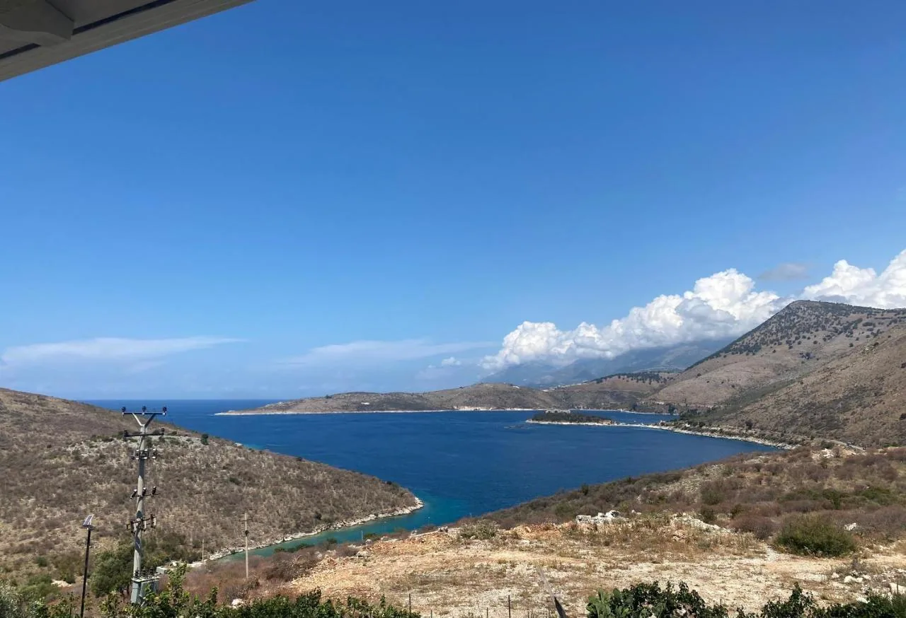 The bay of Porto Palermo seen from the property: a narrow green inlet in the foreground, the open Ionian beyond, bare hills either side
