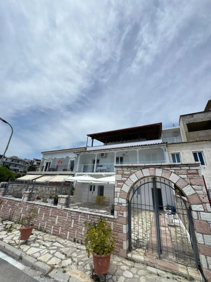 AngelView Apartments seen from Rruga 2 Dhjetori: white walls, a covered veranda, balconies and the pink-grey stone boundary wall with its arched gate