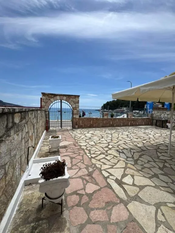 The flagstone terrace at AngelView Apartments end to end, with the arched gate, the beach, the harbour and the mountains across the bay