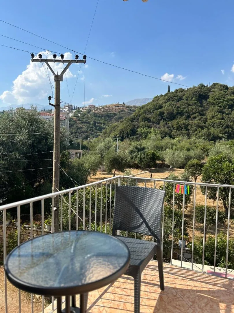 Balcony at Areti Rooms Hotel with a glass table and chair looking over an olive grove and the green hillside