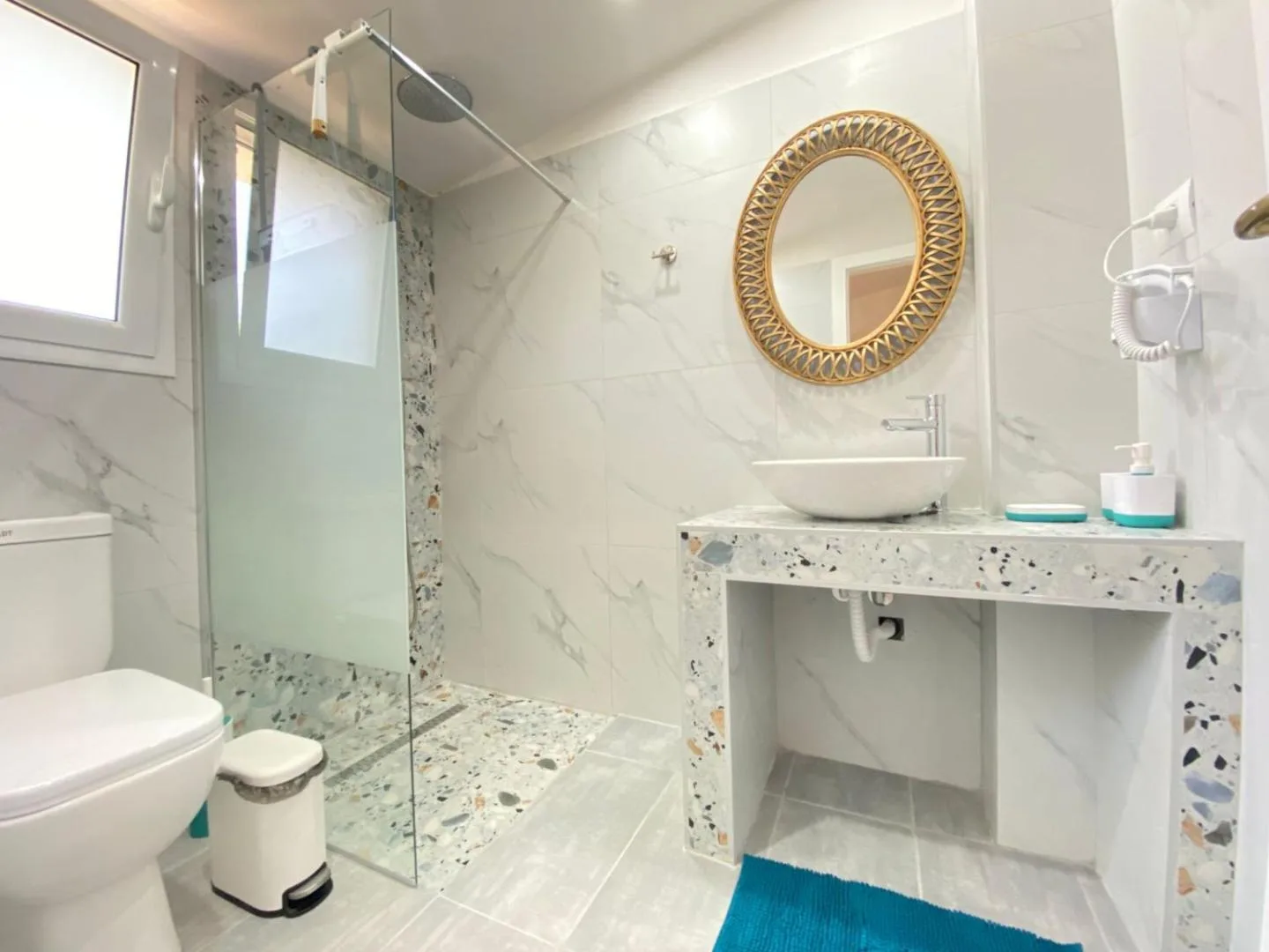 Bathroom at Areti Rooms Hotel with a terrazzo shower floor, terrazzo vanity, vessel basin and a round gilt woven mirror