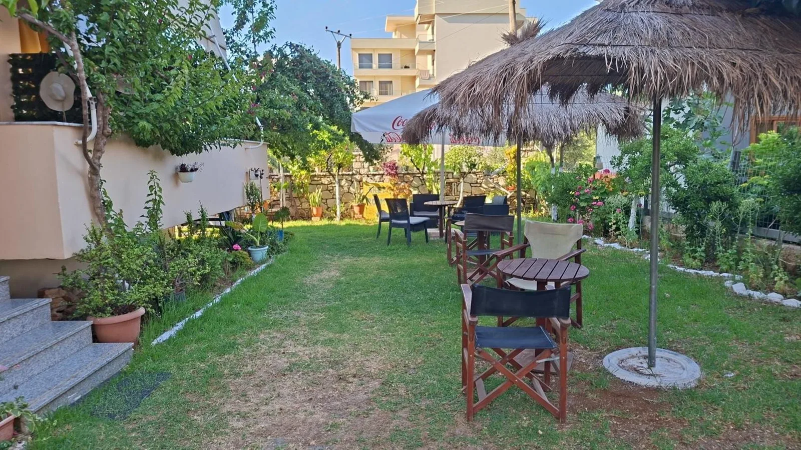 The lawn at Areti Rooms Hotel with thatched parasols, timber director's chairs and a stone garden wall