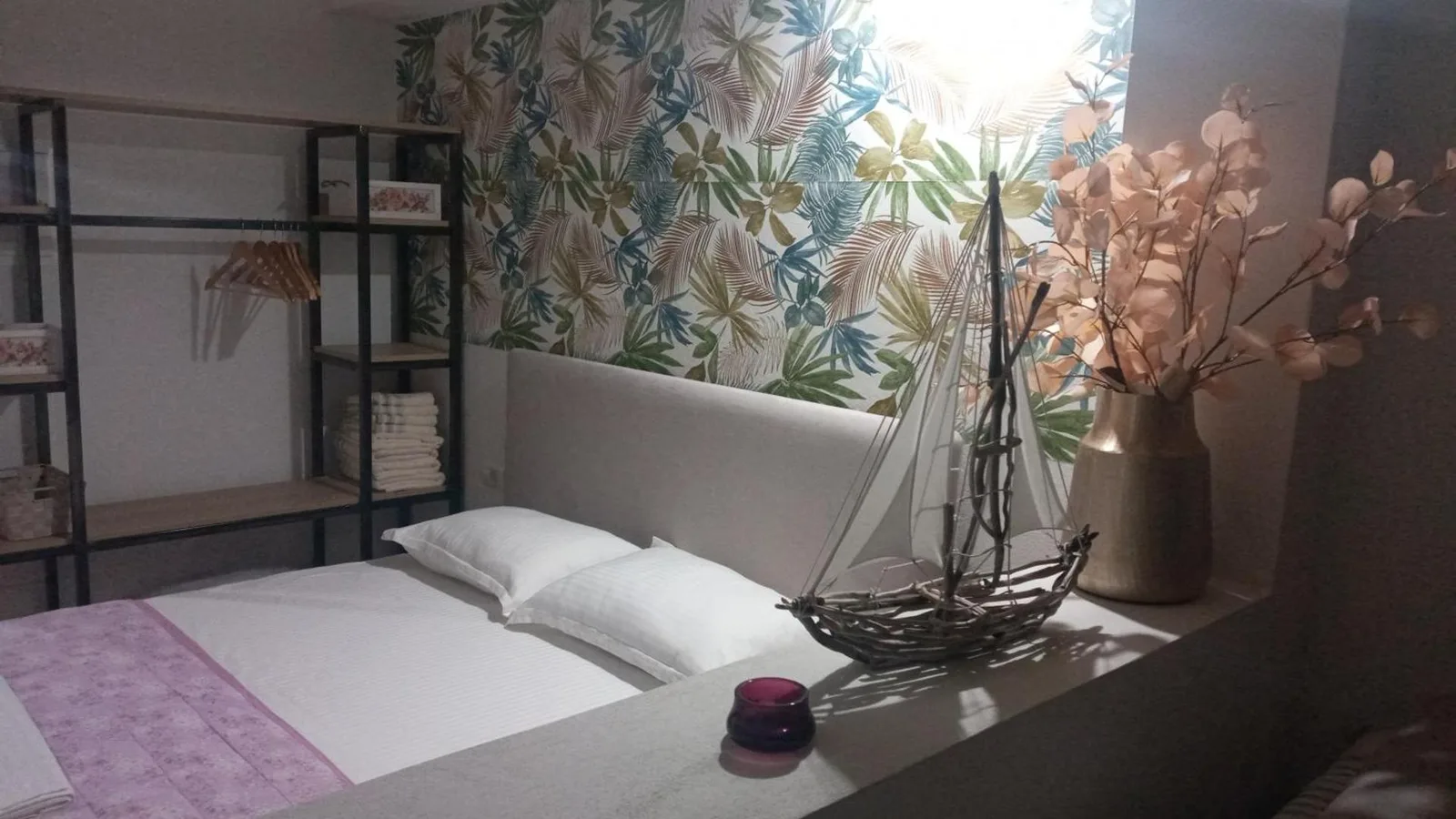 A double room at Areti Rooms Hotel with a palm-print feature wall, an open wardrobe and a driftwood model boat
