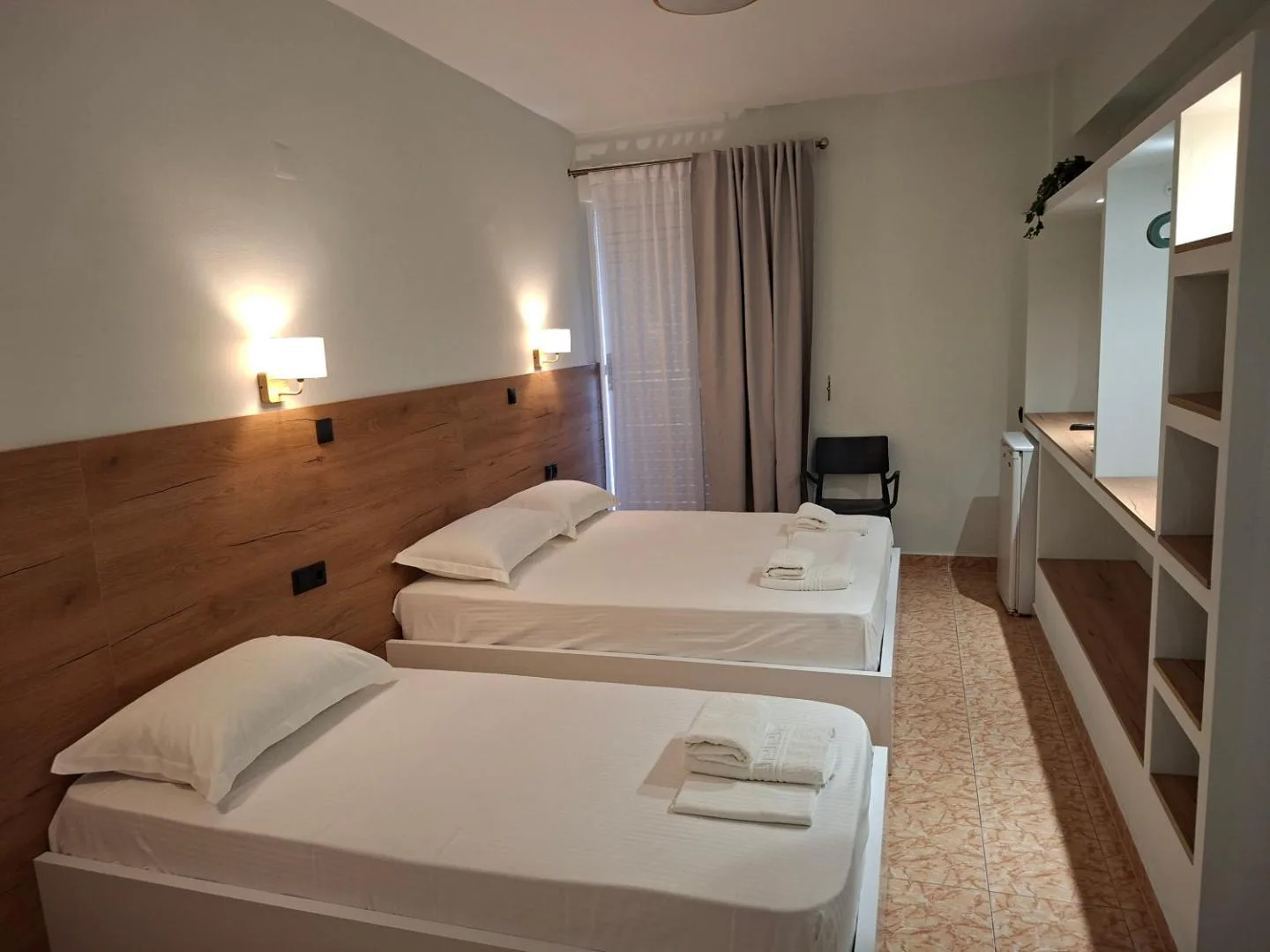 A room at Areti Rooms Hotel with two beds against a full-width oak headboard and two wall lights