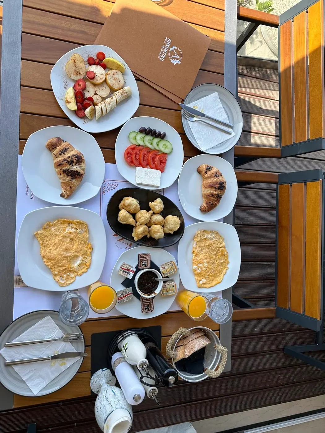 A breakfast spread photographed from above: croissants, omelettes, fried dough balls, tomato, cucumber, olives and white cheese