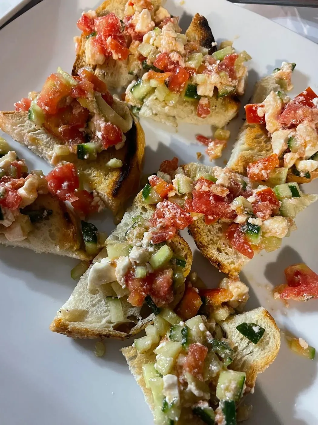 Slices of toasted bread topped with chopped tomato, cucumber and crumbled white cheese