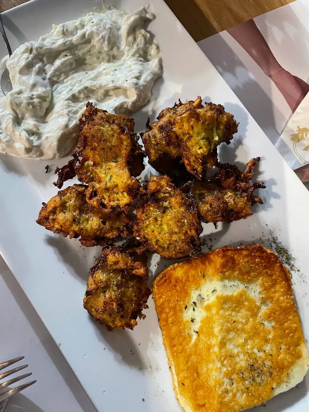 Fried courgette fritters on a white plate with thick yoghurt and a square of fried cheese