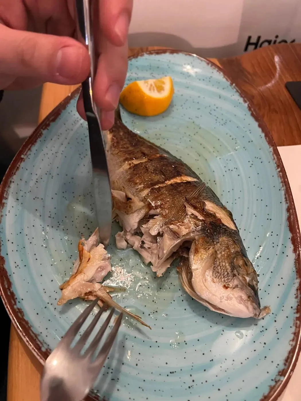 A grilled fish on a pale blue speckled plate, being opened up with a knife and fork