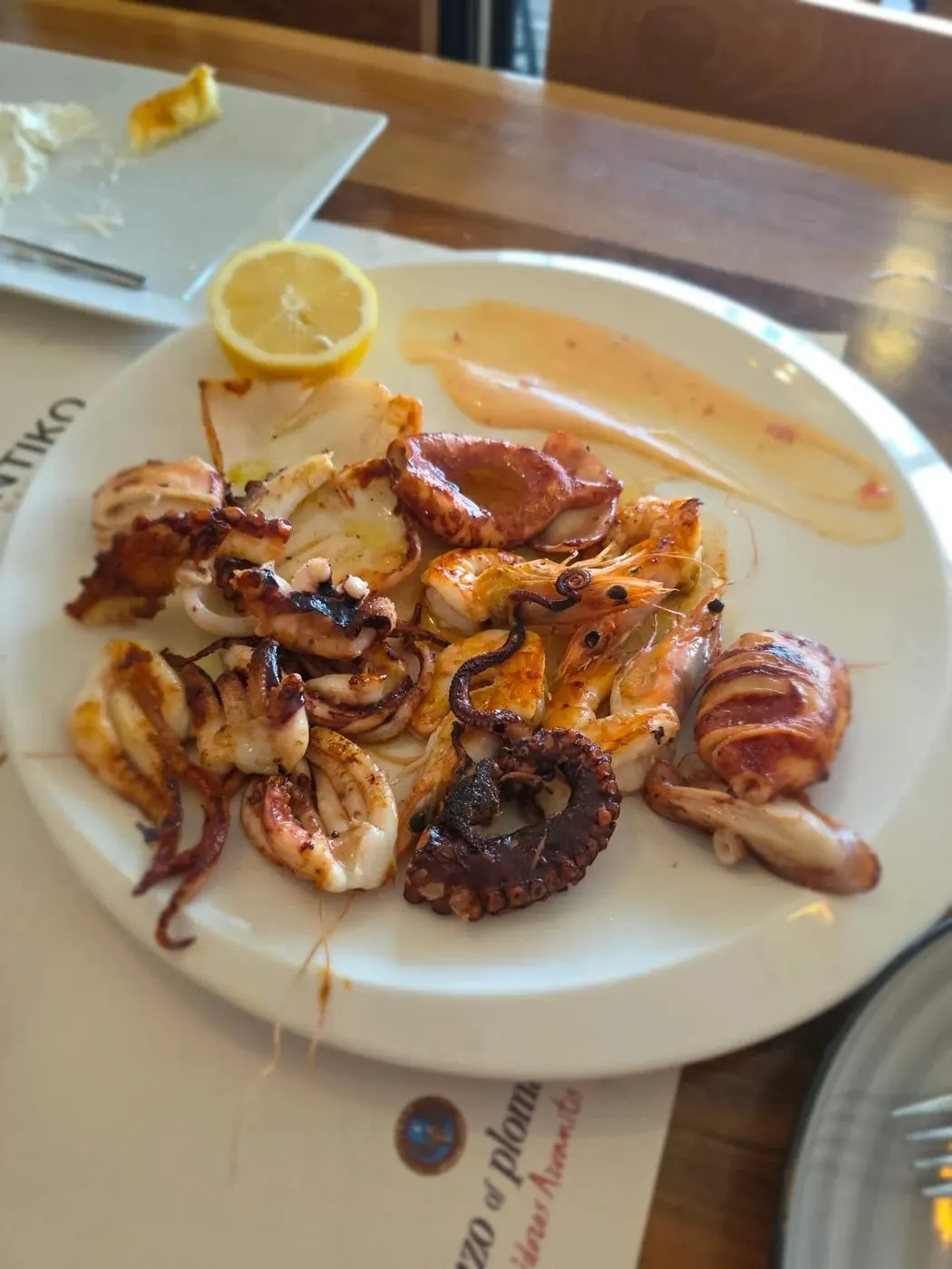Grilled squid, whole prawns and pieces of octopus on a white plate with half a lemon