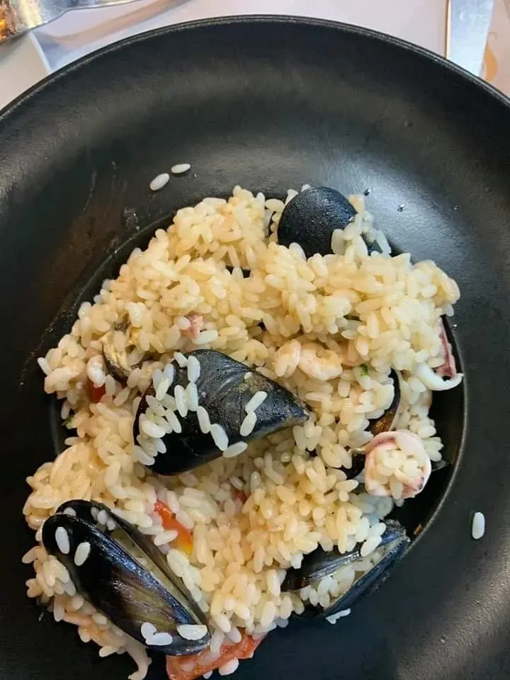 Rice with black mussels in the shell, a prawn and rings of squid in a dark pan