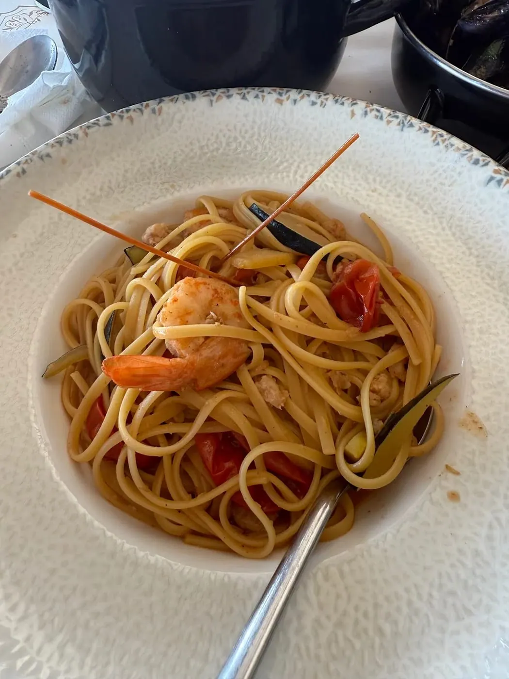 Linguine with a whole prawn, cherry tomatoes and strips of courgette in a white bowl
